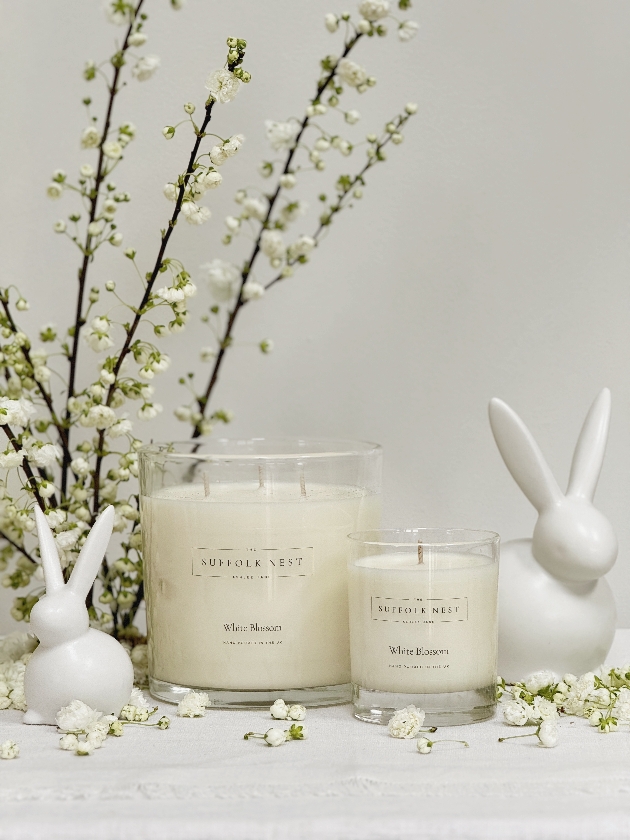 Two cream candles next to two white bunny figures