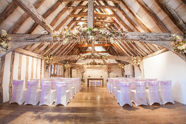 A large barn decorated with flowers and white chairs lining an aisle