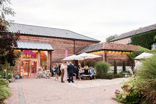 A group of people standing outside of a wooden barn structure decorated with fairylights