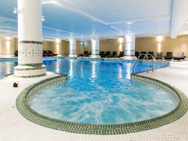 An indoor swimming pool that's decorated with columns and seats around the room