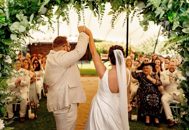 A bride and groom holding hands at the end of an aisle while people cheer