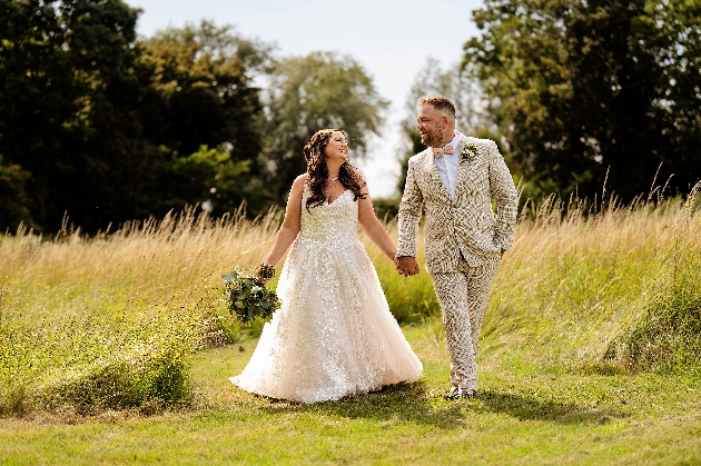 A bride and groom walking hand-in-hand in a field