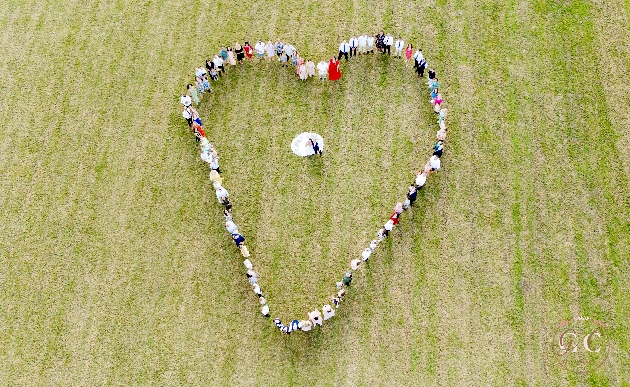 A drone shot of people standing in a heart shape