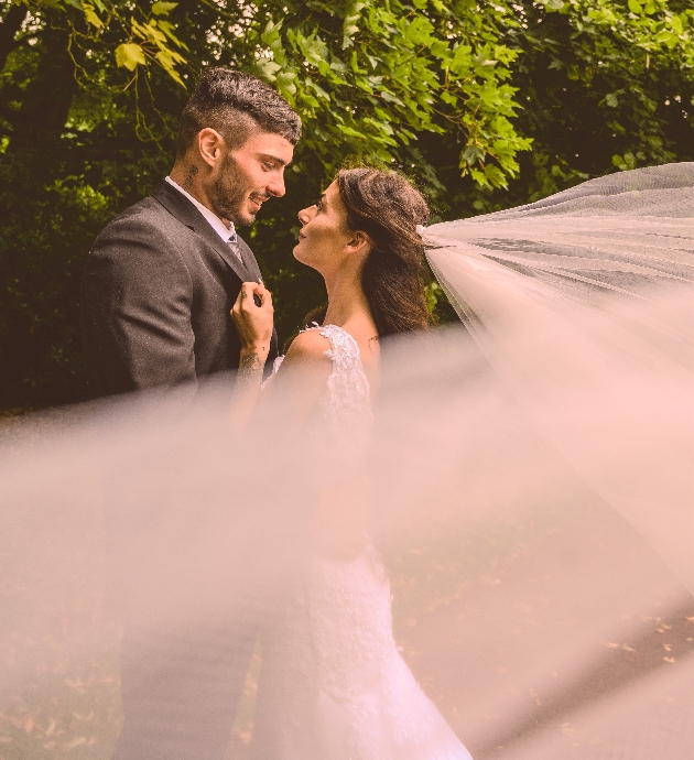 A bride and groom embracing while the bride's veil blows in the wind