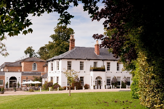 The exterior of a white manor house surrounded by gardens