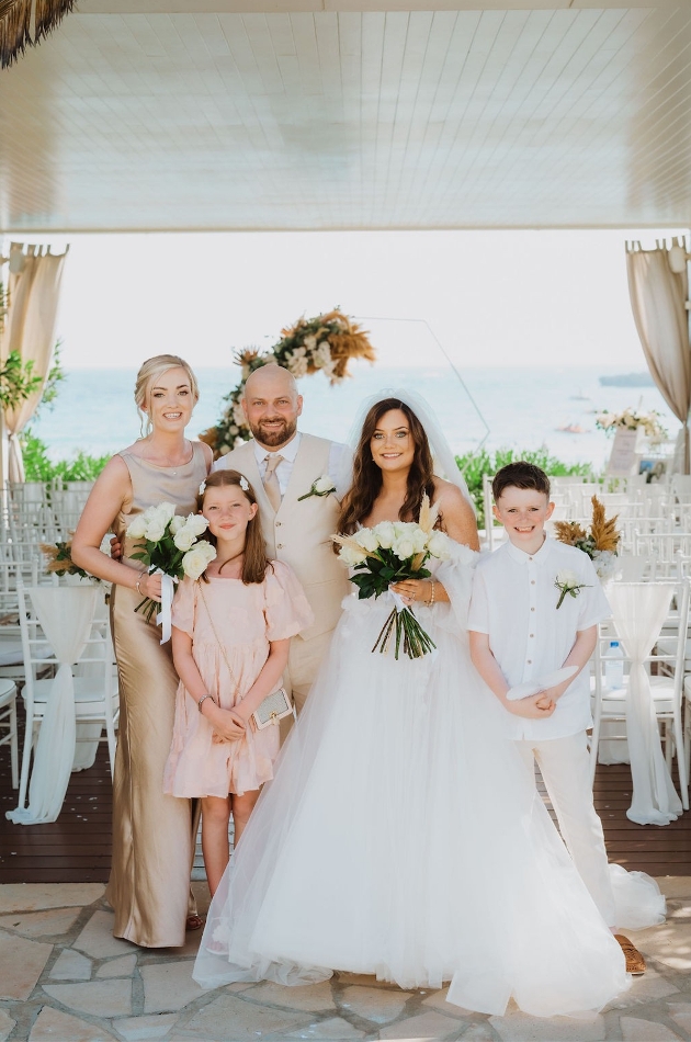 A bride, groom, bridesmaid and two children smiling at the camera