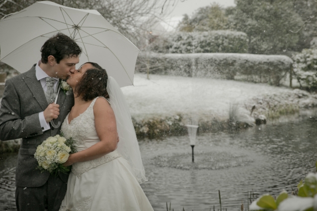 A bride and groom kissing in the snow under an umbrella