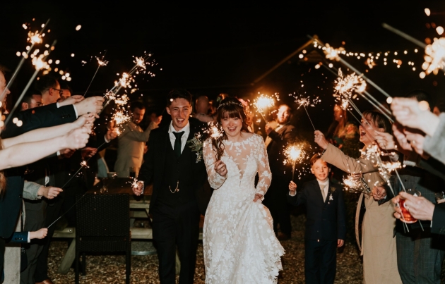 A bride and groom walking through a tunnel of people holding sparklers