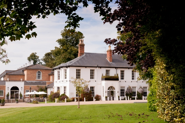 The exterior of a white manor surrounded by trees and grass