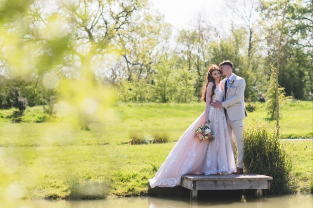 A bride and groom embracing on the side of a lake